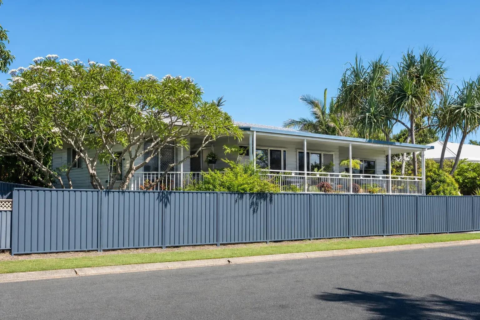 A low-set Australian beach house with painted weatherboard, a wide verandah and established frangipani in the garden