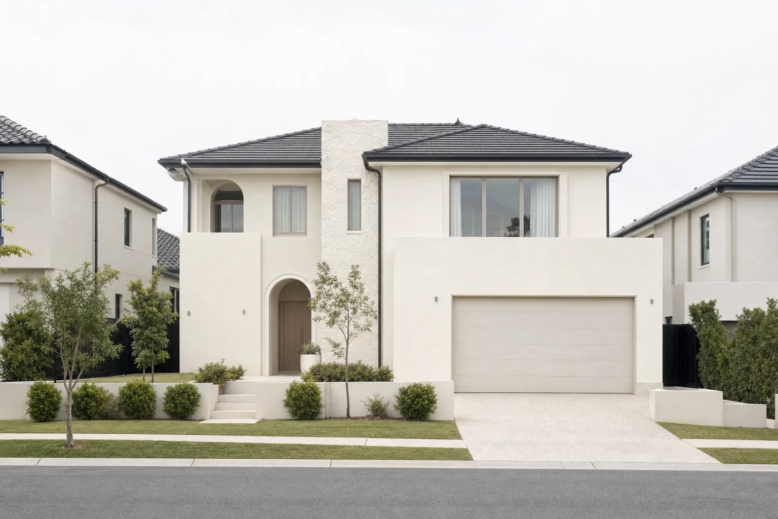 A new two storey rendered Australian estate house with a dark tiled roof, a double garage and young trees in the front garden