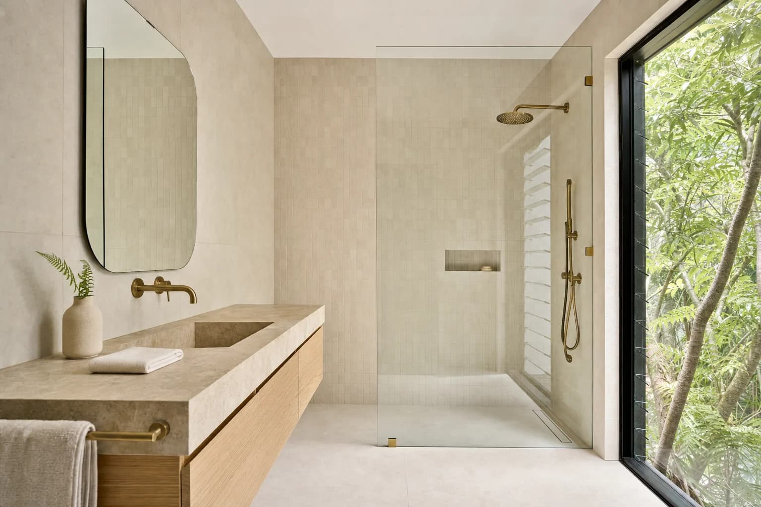 A renovated bathroom in a rural timber home with warm sand tiling, a tan stone benchtop, pale oak joinery and a walk-in shower beside a window