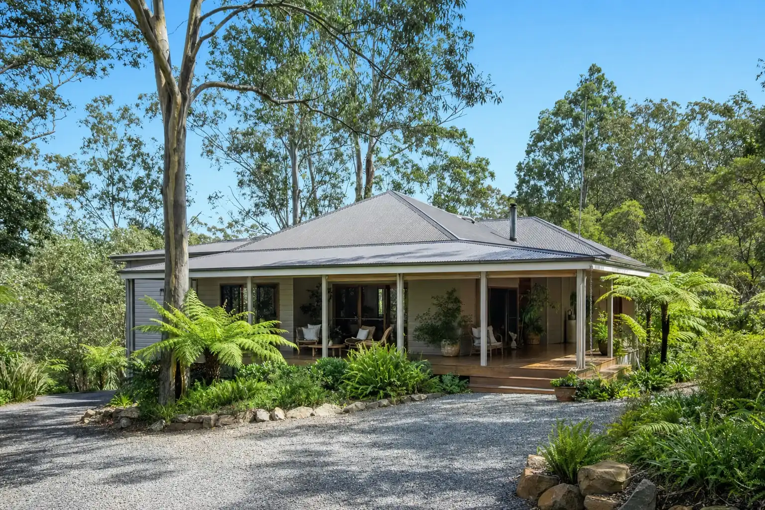 An Australian home on a leafy hinterland block with a wide covered deck, a tin roof and tall eucalypts around it