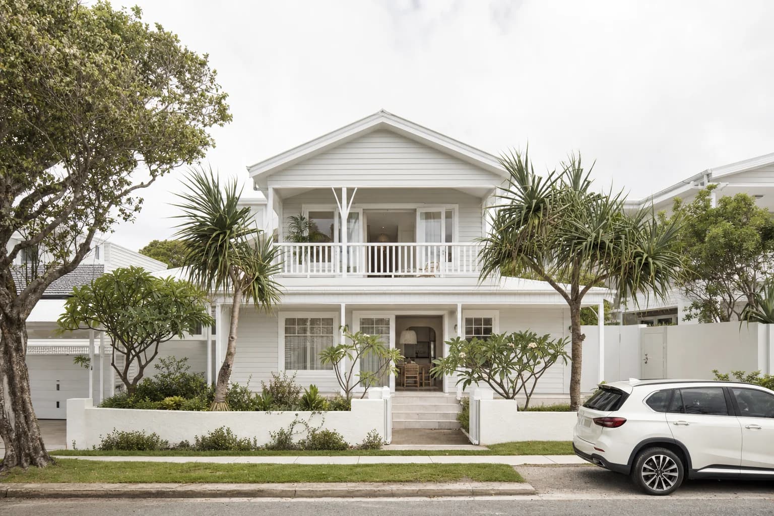 A two storey painted weatherboard beach house with a deep covered deck, white window frames and pandanus in the front garden