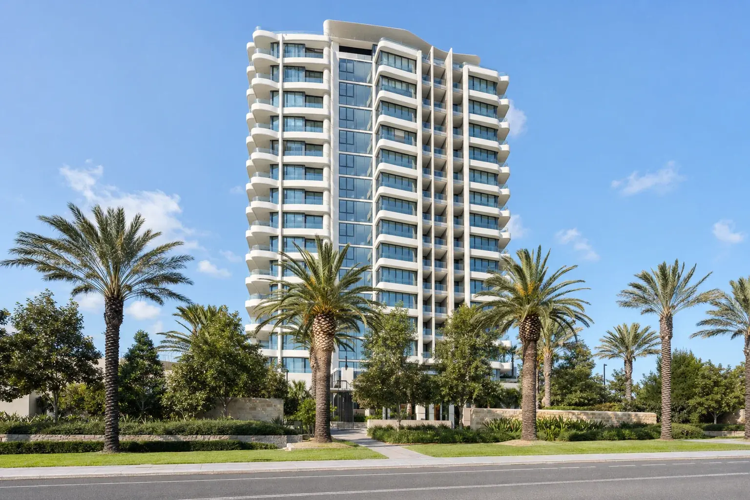 A tall Australian residential tower seen from street level across a landscaped forecourt with mature palms