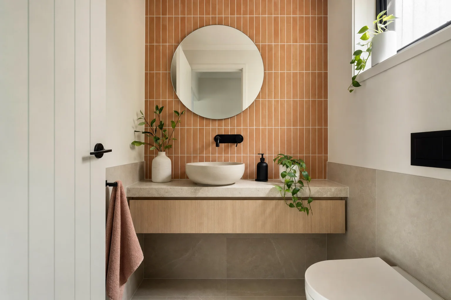 A small renovated Australian powder room with a feature tiled wall, a slim wall-hung vanity and a round mirror